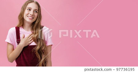 Waist-up shot of delighted charming friendly-looking tender female with cute white smile in corduroy overalls holding palm on breast and gazing right thankful, being grateful for compliments 97736195