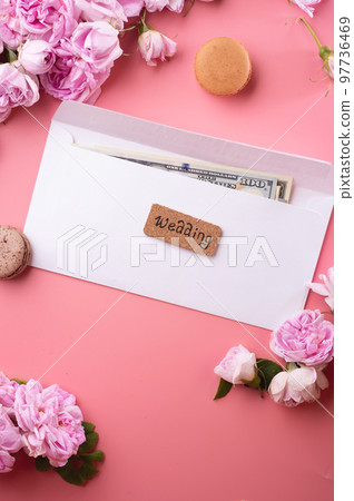 white envelope with cash around roses and macaroons against pink background. life style concept white envelope with cash around roses and macaroons against pink background. life style concept 97736469