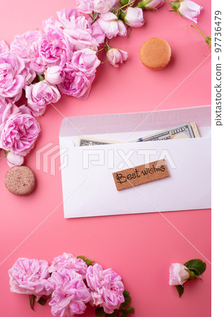white envelope with cash around roses and macaroons against pink background. life style concept white envelope with cash around roses and macaroons against pink background. life style concept 97736479