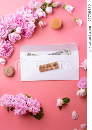 white envelope with cash around roses and macaroons against pink background. life style concept white envelope with cash around roses and macaroons against pink background. life style concept 97736480