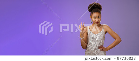Doubtful suspicious clever african-american young woman in silver dress deal cover friend show okay ok confirmation gesture smirking frowning unsure questioned express disbelief hesitation 97736828