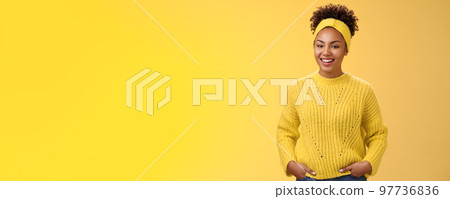 Friendly outgoing relaxed young african-american beautiful girl headband forehead in sweater hold hands pockets smiling broadly have fun talking interesting communication, standing yellow wall 97736836