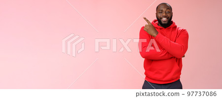 Cheeky outgoing smiling attractive african-american male model in red hoodie grinning energized pointing upper left corner indicating awesome product recommend promo, standing pink background Cheeky outgoing smiling attractive african-american male model in red hoodie grinning energized pointing upper left corner indicating awesome product recommend promo, standing pink background 97737086