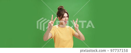 Indoor shot of enthusiastic excited and happy daring girl with combed hair tattoo and cute diasdema showing peace signs bending backwards standing in cool energized pose over green background Indoor shot of enthusiastic excited and happy daring girl with combed hair tattoo and cute diasdema showing peace signs bending backwards standing in cool energized pose over green background 97737158