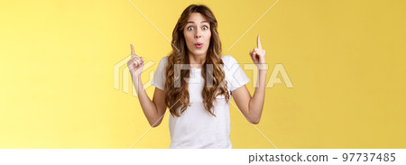 Impressed enthusiastic surprised ambushed cute female model fold lips wow admiration joy stare camera fascinated pointing up index fingers top copy space show you stunning offer yellow background 97737485