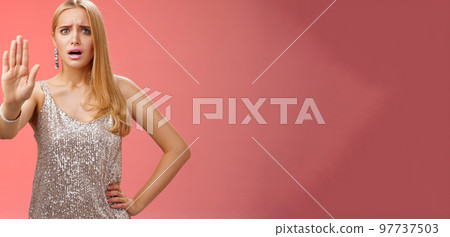 Freaked out displeased bothered insecure blond woman in silver glittering dress extend palm stop enough prohibition rejection gesture bothered pissed annoying clingy man nightclub, red background 97737503