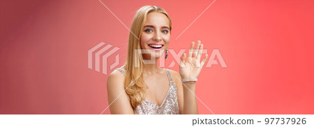 Waist-up studio shot friendly attractive elegant tender blond woman say hi waving raised hand greeting welcoming friend smiling delighted introducing herself hello gesture, red background Waist-up studio shot friendly attractive elegant tender blond woman say hi waving raised hand greeting welcoming friend smiling delighted introducing herself hello gesture, red background 97737926