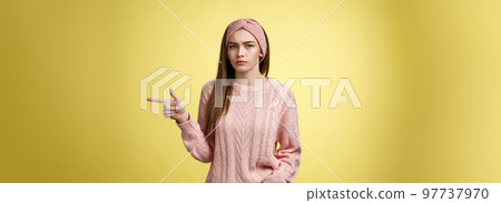 Pissed puzzled young attractive arrogant moody girlfriend in sweater, headband looking irritated, intense frowning pointing finger at copy space, directing person sits on her place, annoyed Pissed puzzled young attractive arrogant moody girlfriend in sweater, headband looking irritated, intense frowning pointing finger at copy space, directing person sits on her place, annoyed 97737970
