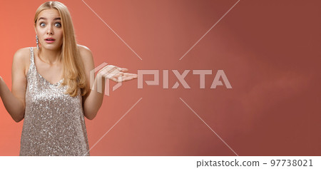 Unsure clueless awkward attractive blond european woman in silver glamour dress shrugging hands sideways widen eyes raise eyebrows unaware no idea what happening, standing questioned confused 97738021