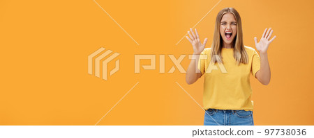Woman releasing stress yelling with joy and pleasure gesturing with raised arms being daring and rebellious not afraid to show emotions standing passionate and expressive against orange background 97738036
