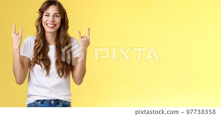 Happy cheerful feminine caucasian girl curly hairstyle show rock-n-roll heavy metal gesture smiling broadly enjoy awesome concert atmosphere stand yellow background joyfully cheering satisfied Happy cheerful feminine caucasian girl curly hairstyle show rock-n-roll heavy metal gesture smiling broadly enjoy awesome concert atmosphere stand yellow background joyfully cheering satisfied 97738358