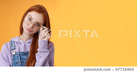 Annoyed bossy unimpressed bothered young redhead female coworker smirking tilting head irritated touch glasses look ignorant cringing stupid uninteresting doubtful story not buy any excuses 97738469