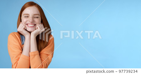 Silly cute happy redhead girlfriend smiling broadly close eyes dreamy squeez cheeks delighted asked date guy likes standing blue background rejoicing have fantastic lucky day triumphing 97739234