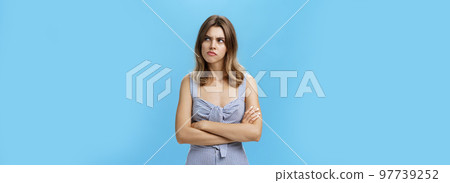Studio shot of woman thinking seriously being suspicious and hesitant pursing lips holding hands crossed on chest looking at upper right corner with frown, thinking over blue background Studio shot of woman thinking seriously being suspicious and hesitant pursing lips holding hands crossed on chest looking at upper right corner with frown, thinking over blue background 97739252