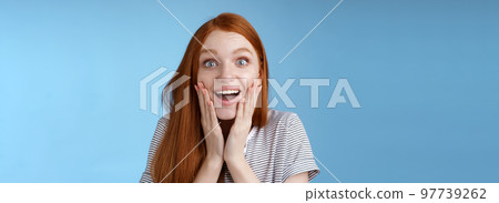 Amused happy dreamy young excited redhead female fan looking fascinated camera smiling admiration delighted touch face thrilled express emotional cheerful surprise, blue background Amused happy dreamy young excited redhead female fan looking fascinated camera smiling admiration delighted touch face thrilled express emotional cheerful surprise, blue background 97739262