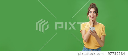 Surprised touched and impressed beautiful european girl with diastema smiling broadly touching cheek from amazement and joy holding smartphone looking happy at camera after reading cool news 97739284