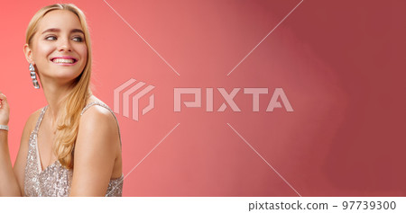 Elegant glamour gorgeous young rich blond woman attend charity party in stylish silver glittering dress accessorize turning right smiling greeting familiar person grinning joyfully, red background 97739300