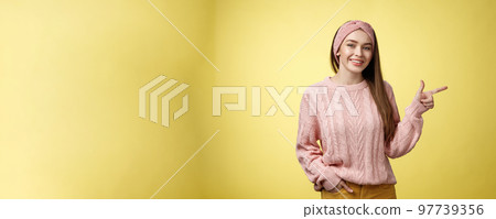 Lifestyle, people, pointing concept. Attractive young girl with long straight hair wearing sweater pointing aside using fore finger, indicating copy space smiling cheerful, positive over yellow wall 97739356