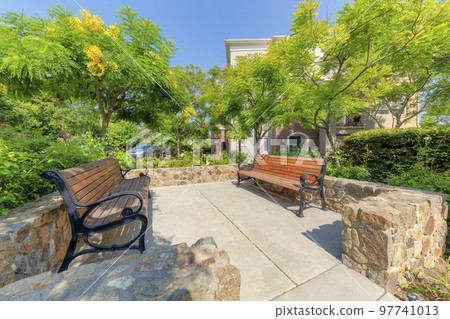Small park with two benches at the front of a two-storey house with arched entryway and blue door 97741013