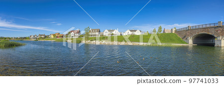 Panoramic view of Oquirrh Lake with grassy shore and stone bridge on the left 97741033