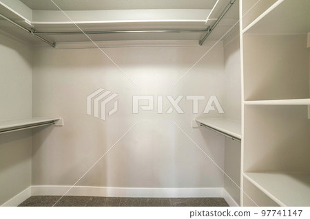 Windowless empty walk-in closet with vertical framed shelves on the right 97741147