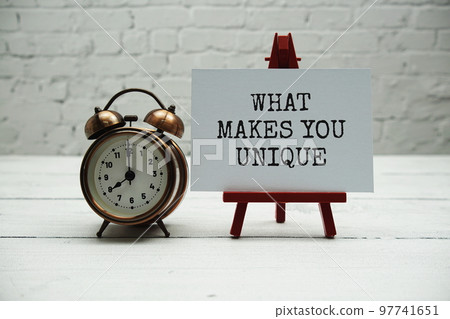 What makes you unique?  text and alarm clock on white brick wall and wooden background 97741651