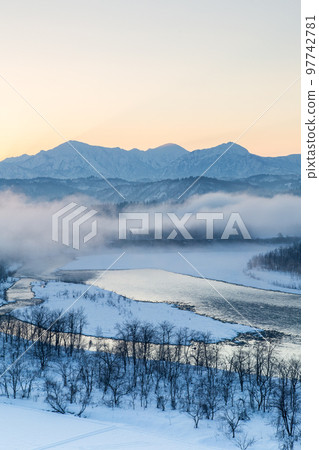 新潟縣小千谷市信濃川和越後三山的雪景，朝霞在霧中反射在水面上 97742781