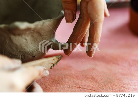 Women's hands knead the clay and sculpt a cup or bowl from it. The process of manufacturing a ceramic product,close up Women's hands knead the clay and sculpt a cup or bowl from it. The process of manufacturing a ceramic product,close up 97743219