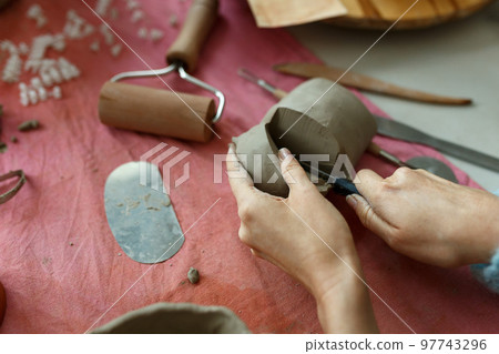 Adult potter master cutting the clay on table. Top view, closeup, hands only. Art and business, hobby and freelance working concept Adult potter master cutting the clay on table. Top view, closeup, hands only. Art and business, hobby and freelance working concept 97743296