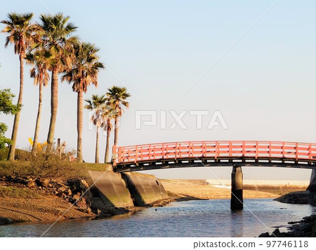 Red arch bridge on seaside lined with palm trees 97746118