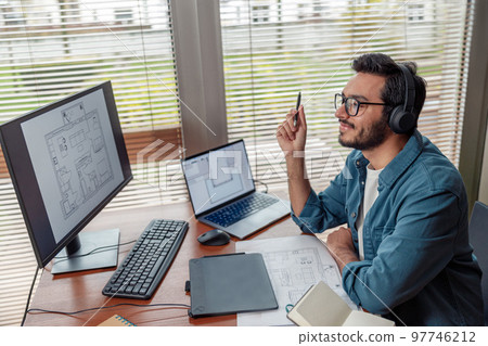 indian male designer in headphones works in home office drawing on graphic tablet 97746212