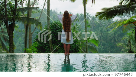 Rear view of long-haired girl enjoys the morning in rice terraces tropical nature background. Woman touches her thick and healthy hair with hands. Summertime nature paddy field. Outdoor landscape. Rear view of long-haired girl enjoys the morning in rice terraces tropical nature background. Woman touches her thick and healthy hair with hands. Summertime nature paddy field. Outdoor landscape. 97746443