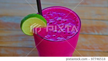 Pitaya dragon fruit smoothie fresh juice beverage drink on a wooden table background. Lime slice and black plastic straw. Close-up, handheld footage. Pitaya dragon fruit smoothie fresh juice beverage drink on a wooden table background. Lime slice and black plastic straw. Close-up, handheld footage. 97746518