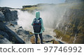Woman standing at stony cliff edge enjoying impressive Detifoss waterfall in Iceland 97746992