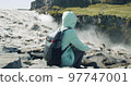 Woman sitting at cliff edge Defocused running river falling into Detifoss waterfall in background Iceland 97747001