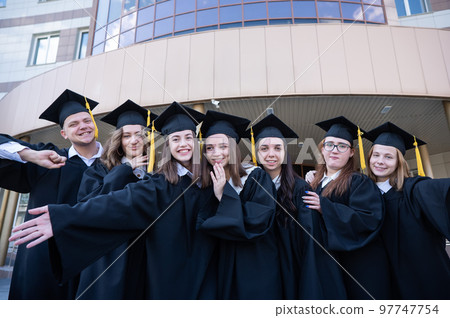 Happy students in graduate gown stand in a row against the backdrop of the university.  97747754