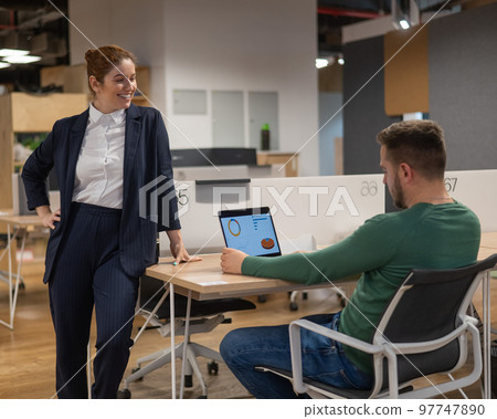 Red-haired caucasian woman and bearded man standing at the desktop. Colleagues discussing work.  97747890