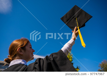 A woman throws her graduation cap against the blue sky. A woman throws her graduation cap against the blue sky. 97747967
