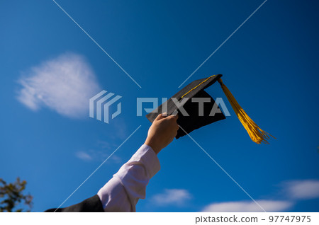 Close-up of a woman's hand with a graduation cap against the blue sky. Close-up of a woman's hand with a graduation cap against the blue sky. 97747975