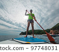 Joyful man is training on a SUP board on a large river during sunny morning. Stand up paddle boarding - awesome active recreation in nature. Backlight. Joyful man is training on a SUP board on a large river during sunny morning. Stand up paddle boarding - awesome active recreation in nature. Backlight. 97748031