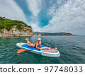 Young beautiful woman relaxing in the sea on a SUP board. The girl sunbathes on the beach of the island on vacation. Young beautiful woman relaxing in the sea on a SUP board. The girl sunbathes on the beach of the island on vacation. 97748033