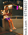 Young woman sitting with her phone on the street at night Young woman sitting with her phone on the street at night 97748037