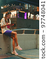 Young woman sitting with her phone on the street at night Young woman sitting with her phone on the street at night 97748041