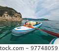 Fit woman in bikini relaxing on a sup surfboard, floating on the clear sea on cliff background Fit woman in bikini relaxing on a sup surfboard, floating on the clear sea on cliff background 97748059