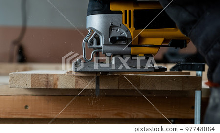 Close-up of a man cutting a wooden plank with an electric jigsaw in a workshop. 97748084