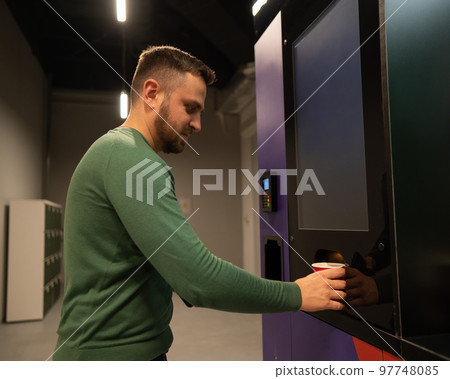 Caucasian man pours himself coffee from a vending machine.  97748085