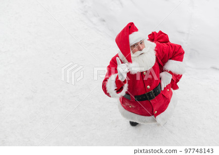Top view on friendly santa claus actively gesturing and wishing merry christmas. An elderly man in a Santa costume stands on the snow outside and wishes a happy new year. 97748143