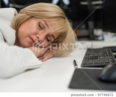 Caucasian blonde woman sleeping at her desk in the office.  97748872