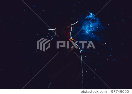 silhouette of a male detective in a hat and raincoat smoking at night 97749000