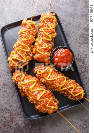 Korean corn dogs are hot dogs coated in a batter, then deep fried and finished with sugar mustard and ketchup closeup on the plate. Vertical top view 97749041